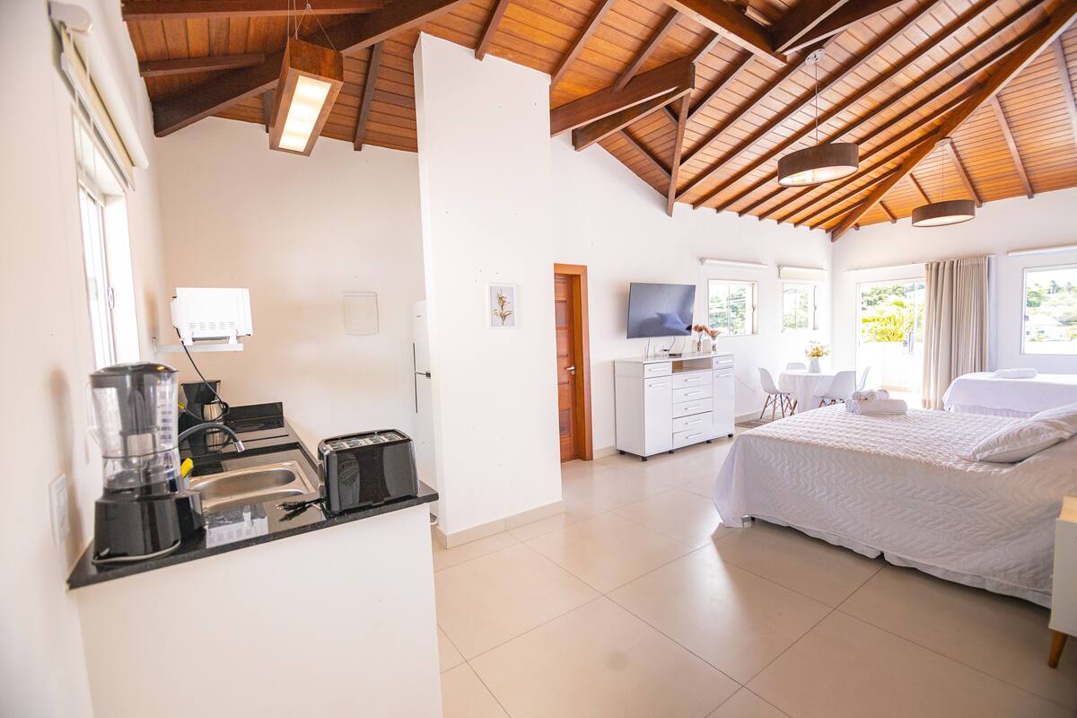 A hotel room with a kitchenette, a bed, a TV, and large windows.