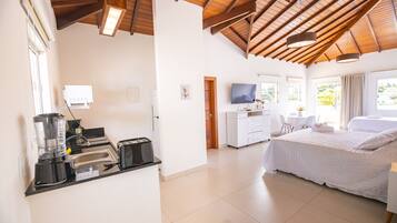 Quarto de hotel com cozinha compacta, cama, televisão e janelas amplas.