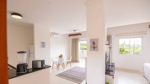 A modern kitchen with a blender and toaster, a dining area with a table and chairs, and a bedroom with a bed and window. - Apart Lagoa Buzios- Centro (Búzios)