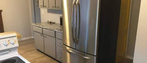 A kitchen with a stainless steel refrigerator, a white stove, and light wood cabinets.