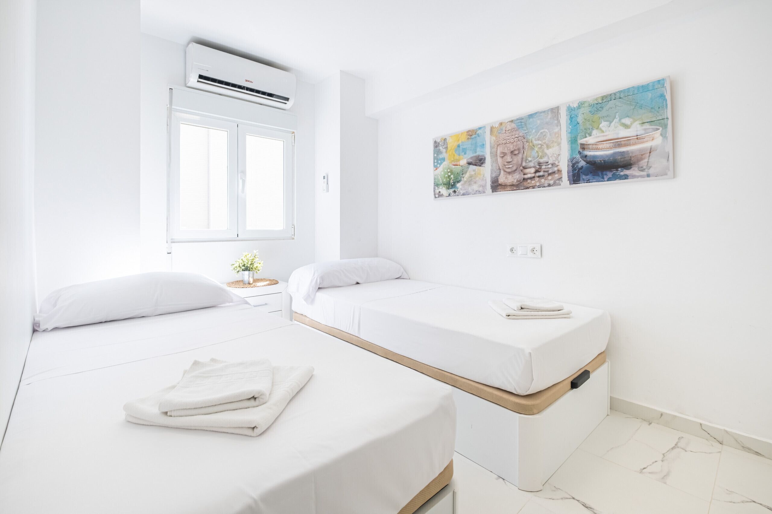Ein modernes Hotelzimmer mit zwei Betten, einem Fenster, einer Klimaanlage und einer Wand mit drei Bildern.