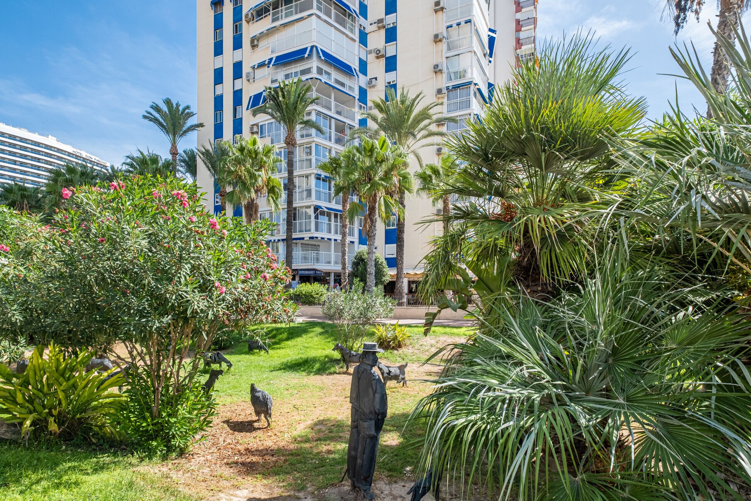 Un patio de hotel con palmeras, una estatua y vistas a un edificio de gran altura con balcones.