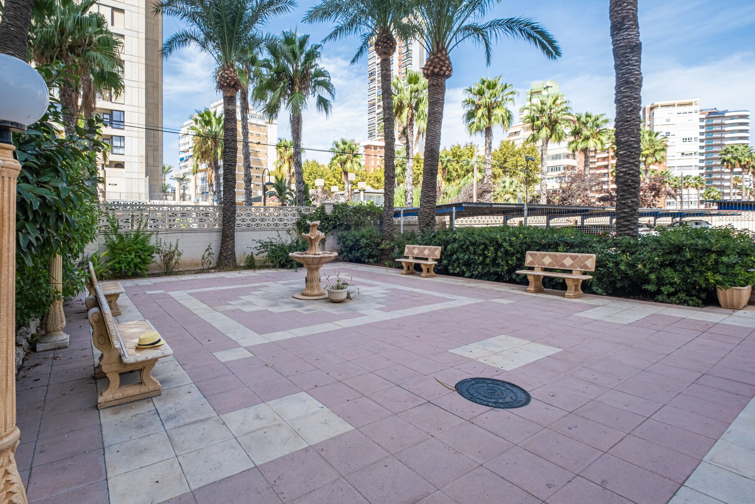 An outdoor courtyard with a fountain, benches, and palm trees.