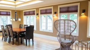 A dining area with a wooden table and chairs, a wicker chair, and a chandelier.