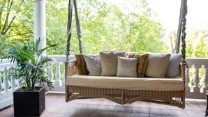 A wicker swing bed with cushions, a potted plant, and a white balustrade.