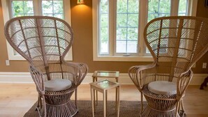 Two wicker chairs with cushions, a small glass table, and a view of a window with a view of greenery outside.