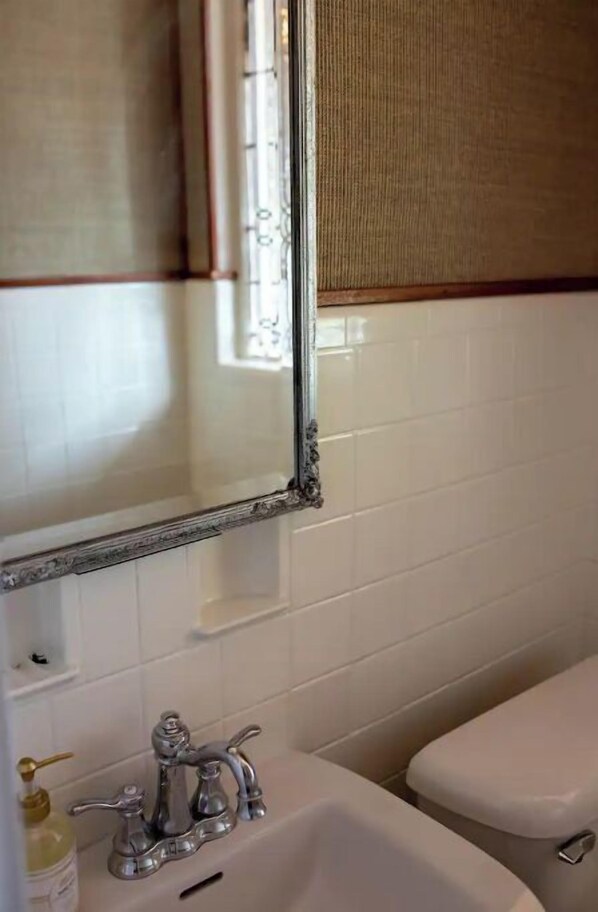 Un baño con pared de azulejos blancos, un grifo plateado, un espejo con marco de madera y una toalla beig colgando de la pared.