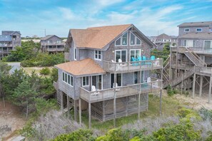 A two-story house with a balcony and a deck, surrounded by trees and other houses. - Oceanfront Dog Friendly Home w/ Hot Tub and Nearby Beach Access (Avon)