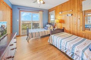 A room with two beds, wooden walls, a ceiling fan, a window with a view, and a wooden dresser. - Oceanfront Dog Friendly Home w/ Hot Tub and Nearby Beach Access (Avon)