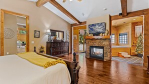 Une chambre spacieuse avec un grand lit, des poutres apparentes, une cheminée et une vue sur le salon.