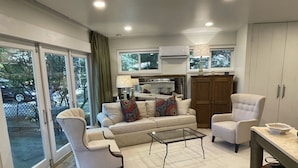A modern living room with a sofa, armchairs, a glass coffee table, and a kitchen area visible through a glass door. - Marble Studio (Highlands)