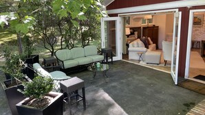 An outdoor patio area with a light green sofa, a wicker chair, and a small table. There are potted plants and a brick wall in the background. - Marble Studio (Highlands)