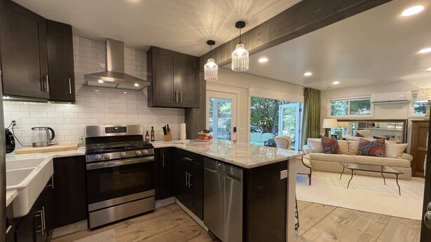 A modern kitchen with dark cabinetry, stainless steel appliances, and a large island. - Marble Studio (Highlands)