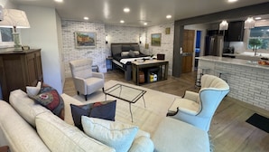A modern living room with a sofa, armchairs, a dining table, and a kitchen area with a refrigerator and sink. - Marble Studio (Highlands)
