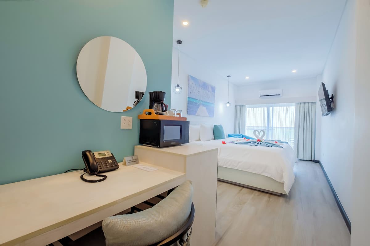 Una habitación de hotel con escritorio, cama, espejo redondo, cafetera y televisor.