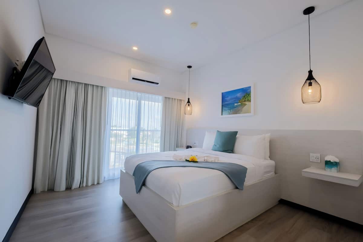 Habitación de hotel moderna con una cama grande, un televisor de pantalla plana, un cuadro y un estante pequeño.
