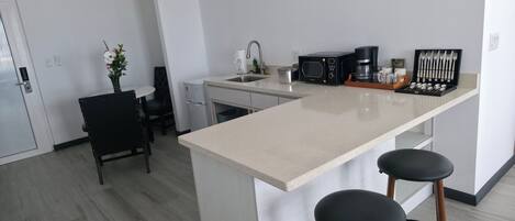 A modern kitchen with a central island, a microwave, a coffee maker, and bar stools.