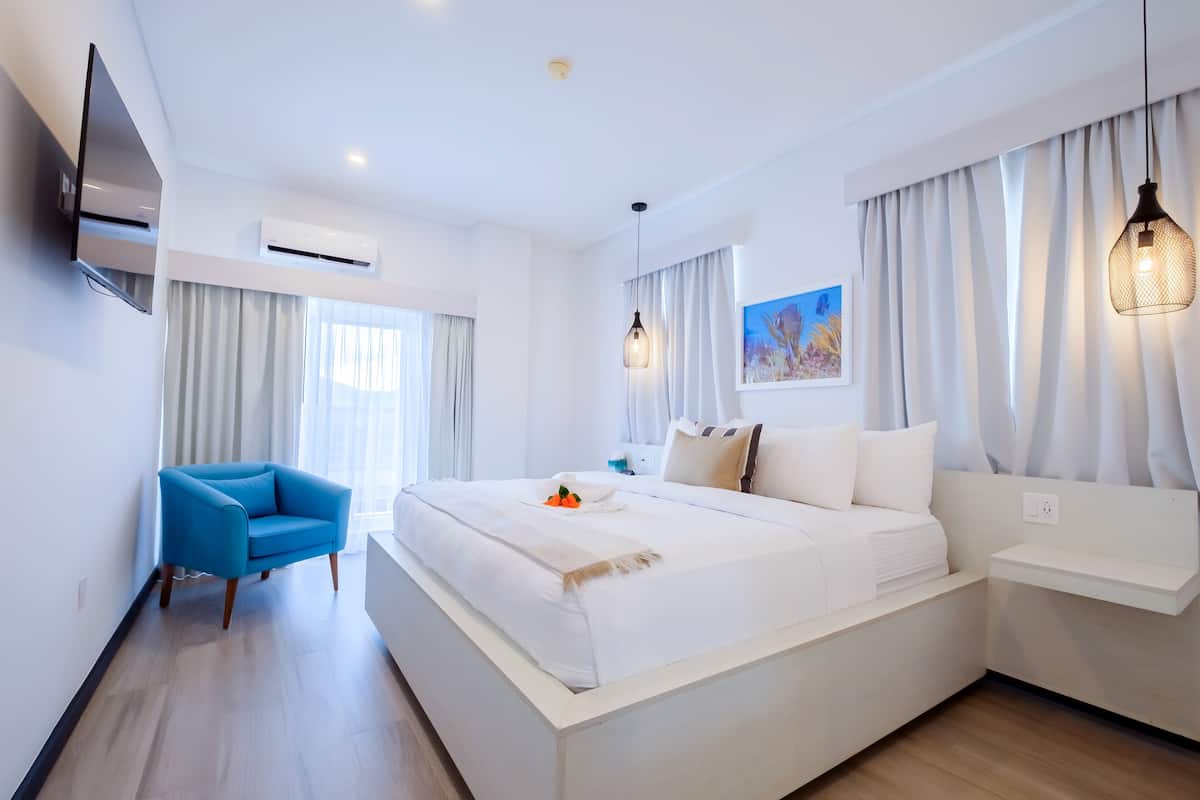 Una habitación de hotel moderna con una cama grande, un sillón azul, un televisor de pantalla plana y un equipo de aire acondicionado.