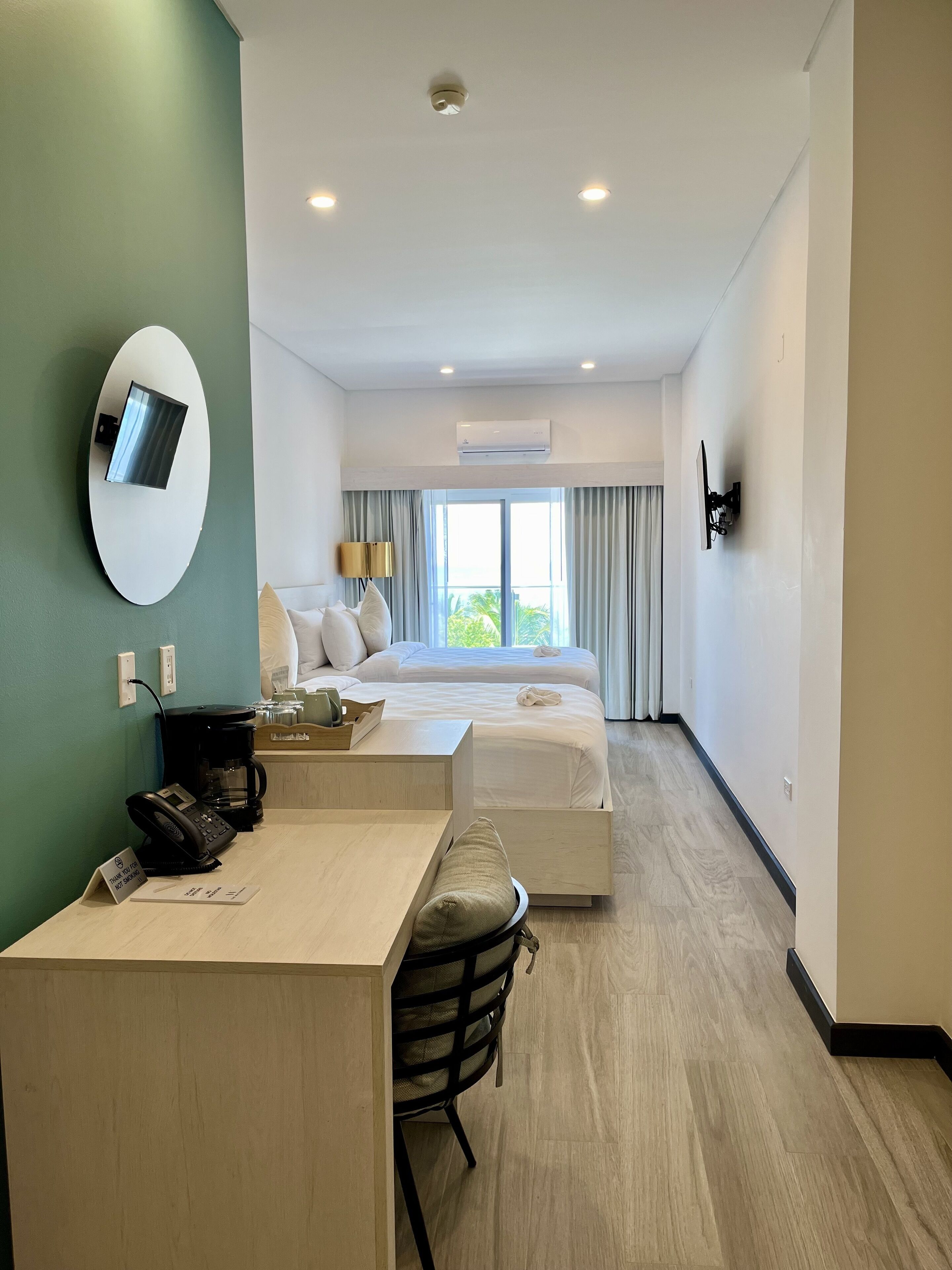 A hotel room with a bed, bedside tables, a desk, a chair, a coffee maker, a phone, a TV, and a window with curtains.