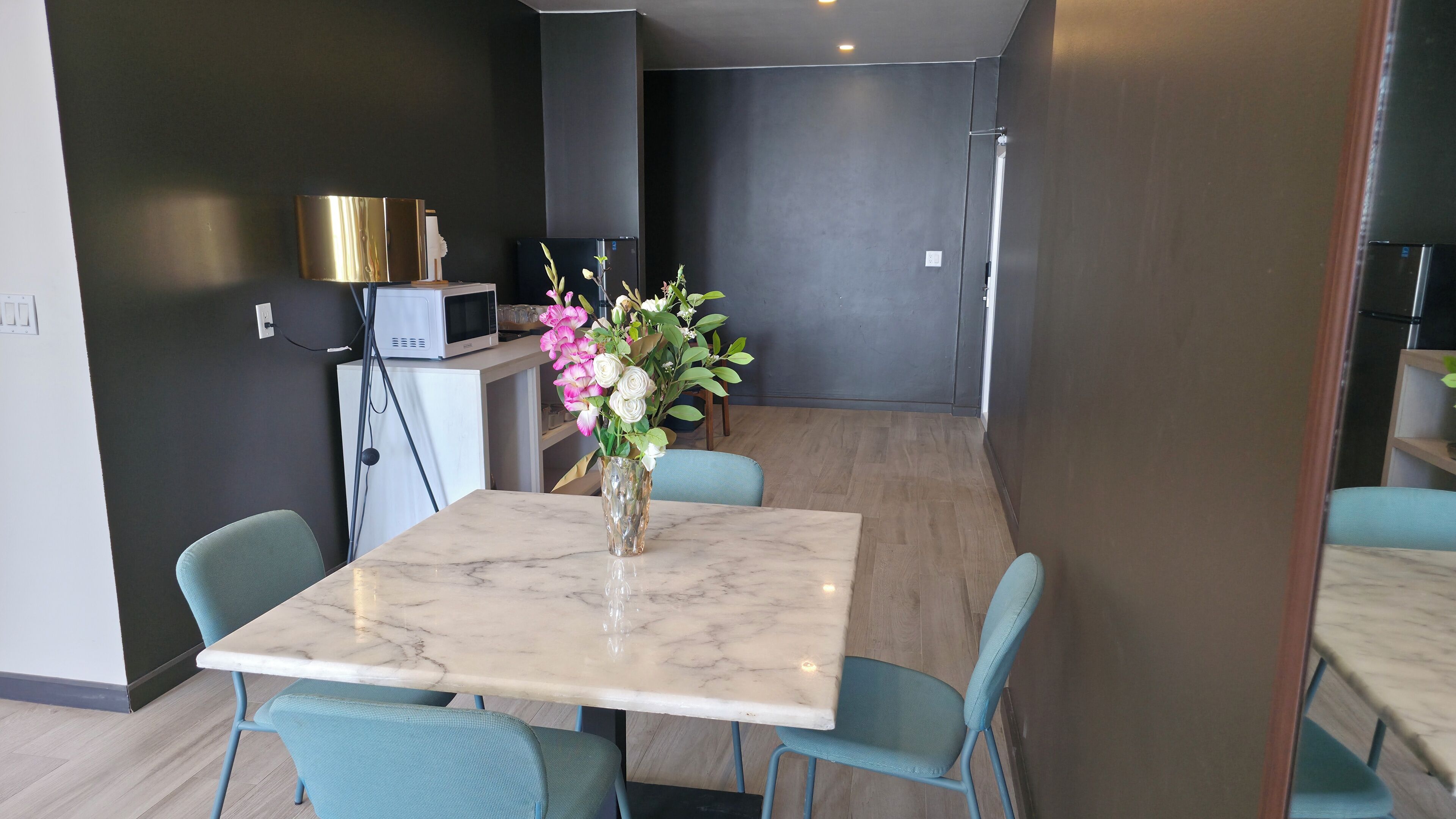Un espace repas moderne avec une table en marbre et des chaises de couleur turquoise, un petit réfrigérateur et un vase rempli de fleurs.