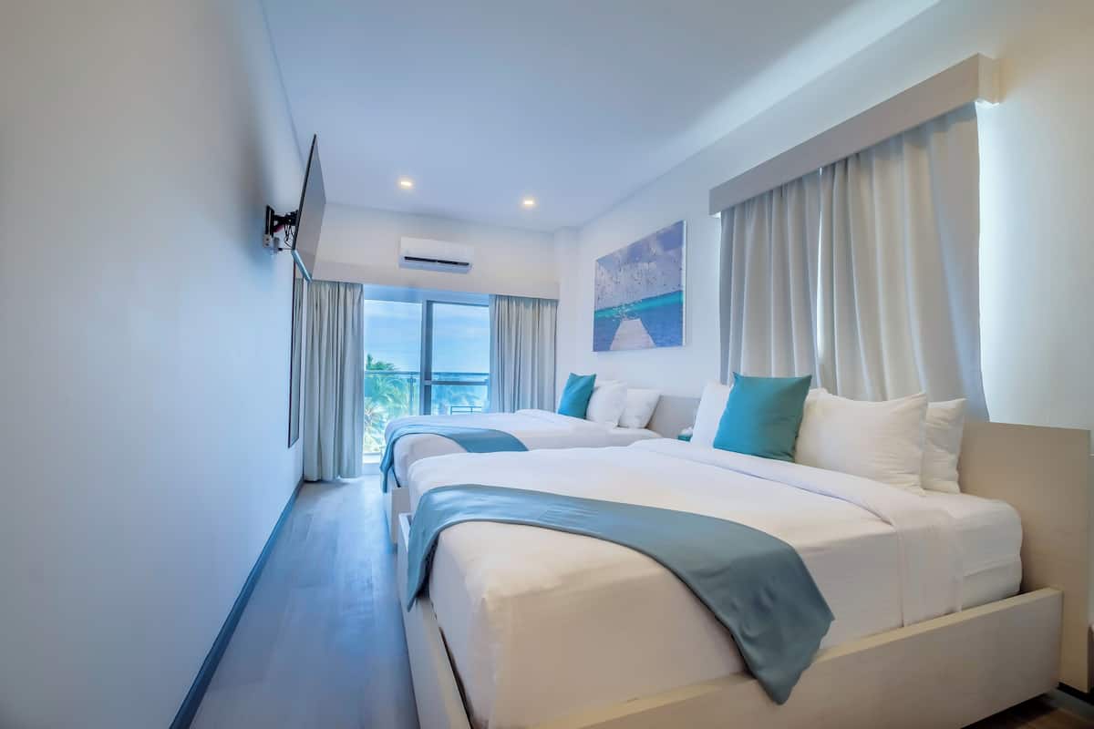 Habitación de hotel con dos camas, un televisor de pantalla plana montado en la pared, un equipo de aire acondicionado y un cuadro en la pared.