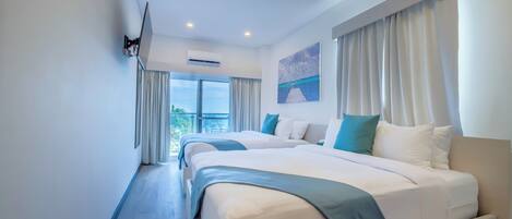 A hotel room with two beds, a flat-screen TV mounted on the wall, an air conditioning unit, and a painting on the wall.