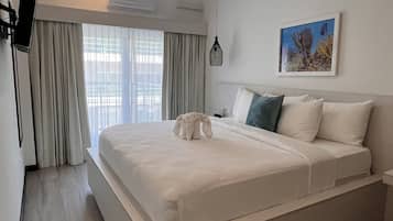 Una habitación de hotel moderna con una cama grande, un televisor de pantalla plana montado en la pared, un aire acondicionado instalado en el techo y un cuadro con vida marina en la pared.