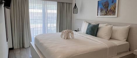 A modern hotel room with a large bed, a flat-screen TV mounted on the wall, a ceiling-mounted air conditioner, and a framed picture of marine life on the wall.