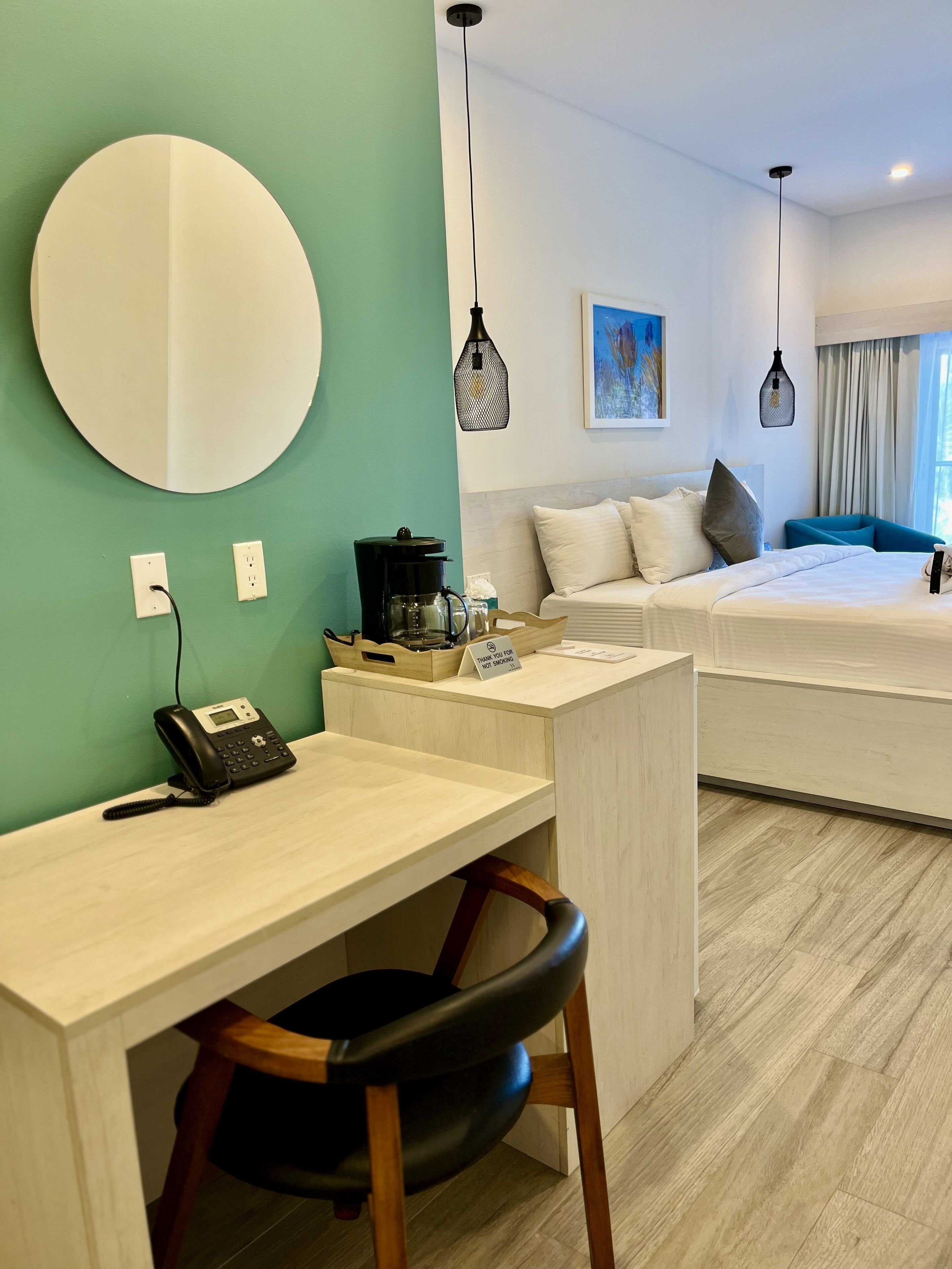Una habitación de hotel con escritorio, una silla, una cama, una cafetera y un cartel que dice 'Gracias por no fumar'.