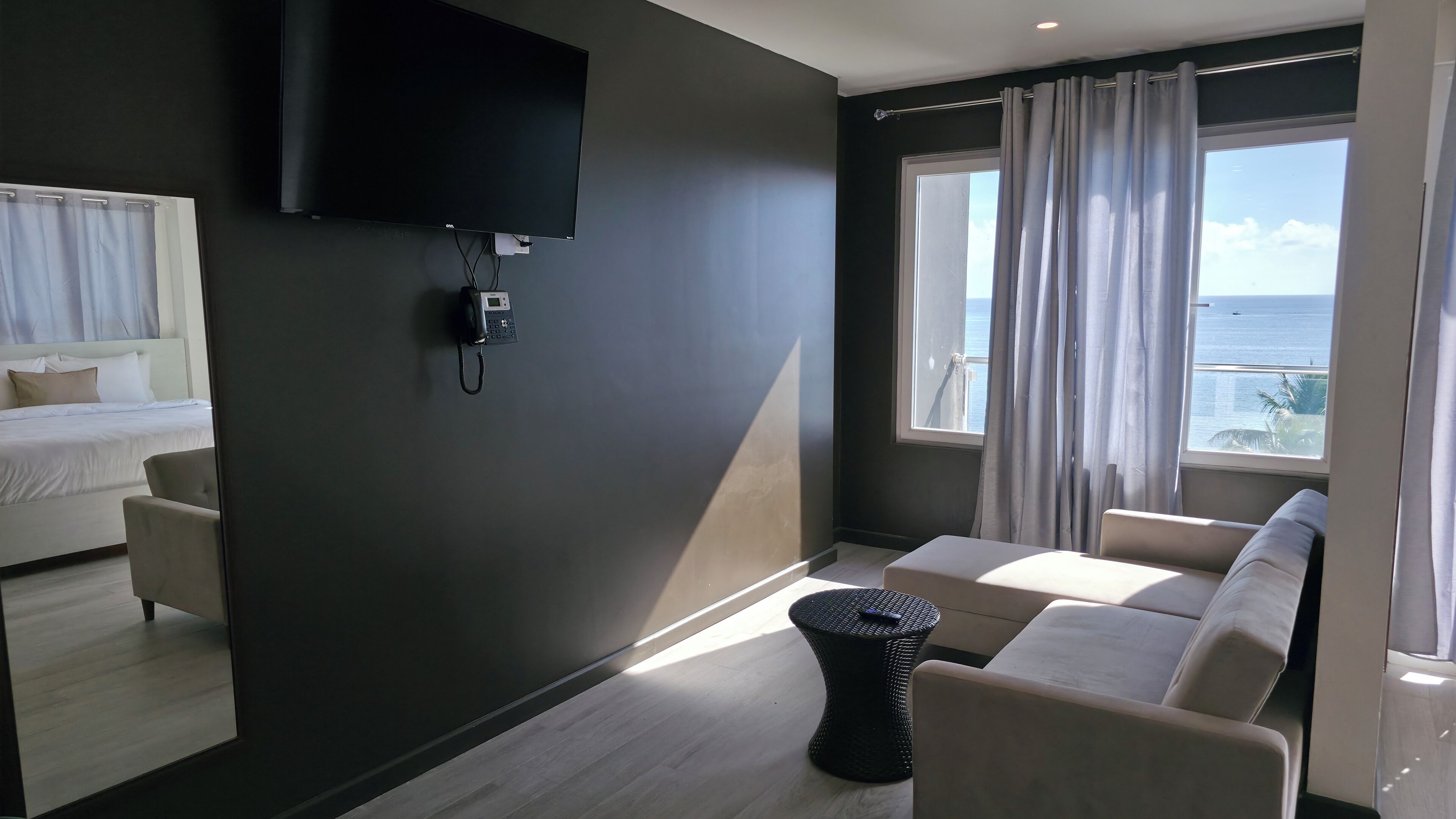Una habitación de hotel moderna con una cama, un sofá, una mesita, un televisor montado en la pared y una ventana con cortinas.
