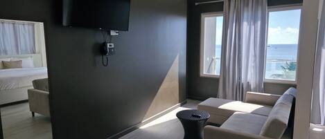 Una habitación de hotel moderna con una cama, un sofá, una mesita, un televisor montado en la pared y una ventana con cortinas.