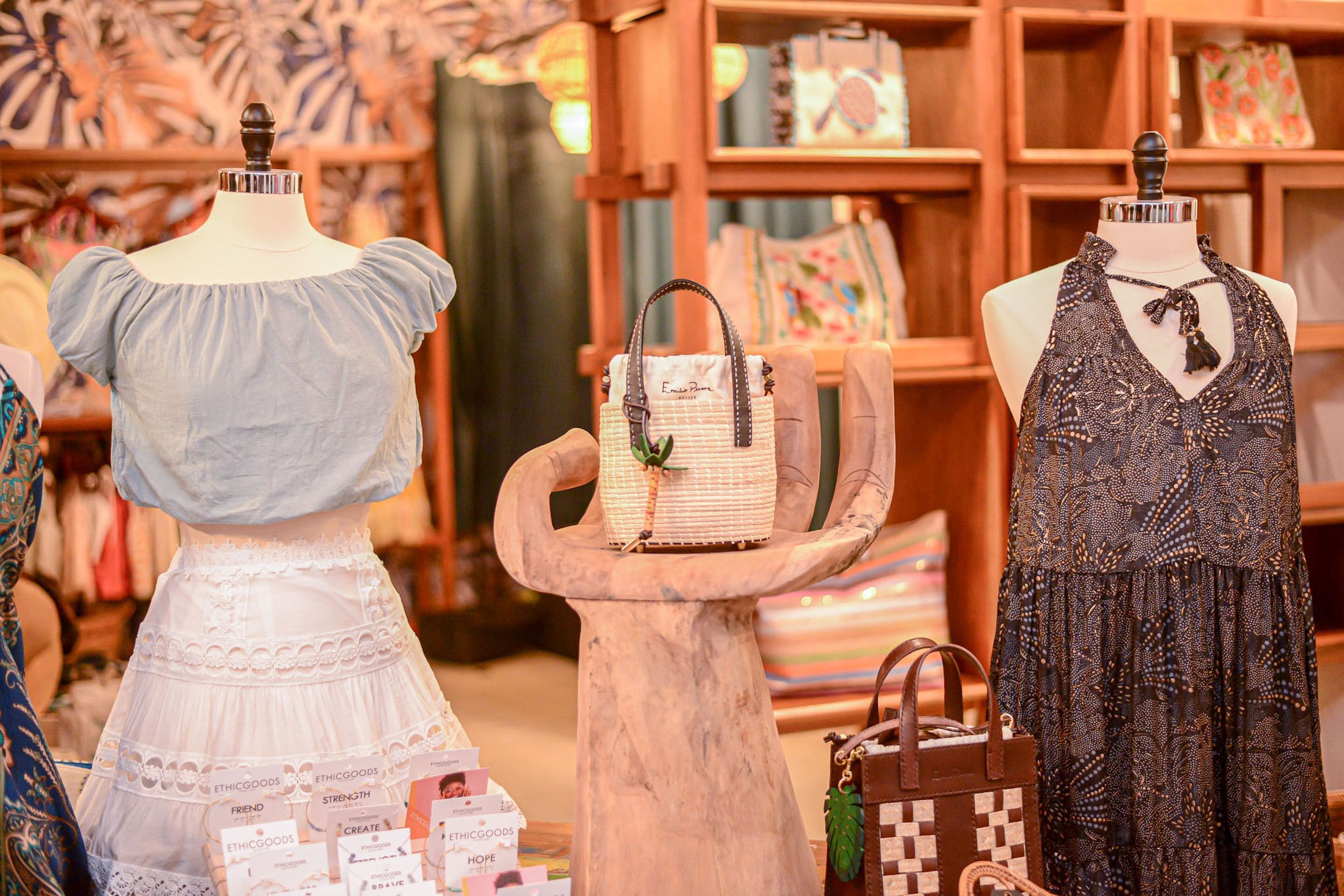 Maniquíes exhiben ropa y bolsos en una tienda con estanterías de madera y papel tapiz estampado.