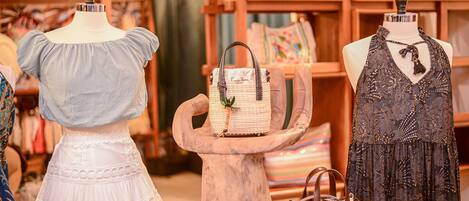 Maniquíes exhiben ropa y bolsos en una tienda con estanterías de madera y papel tapiz estampado.