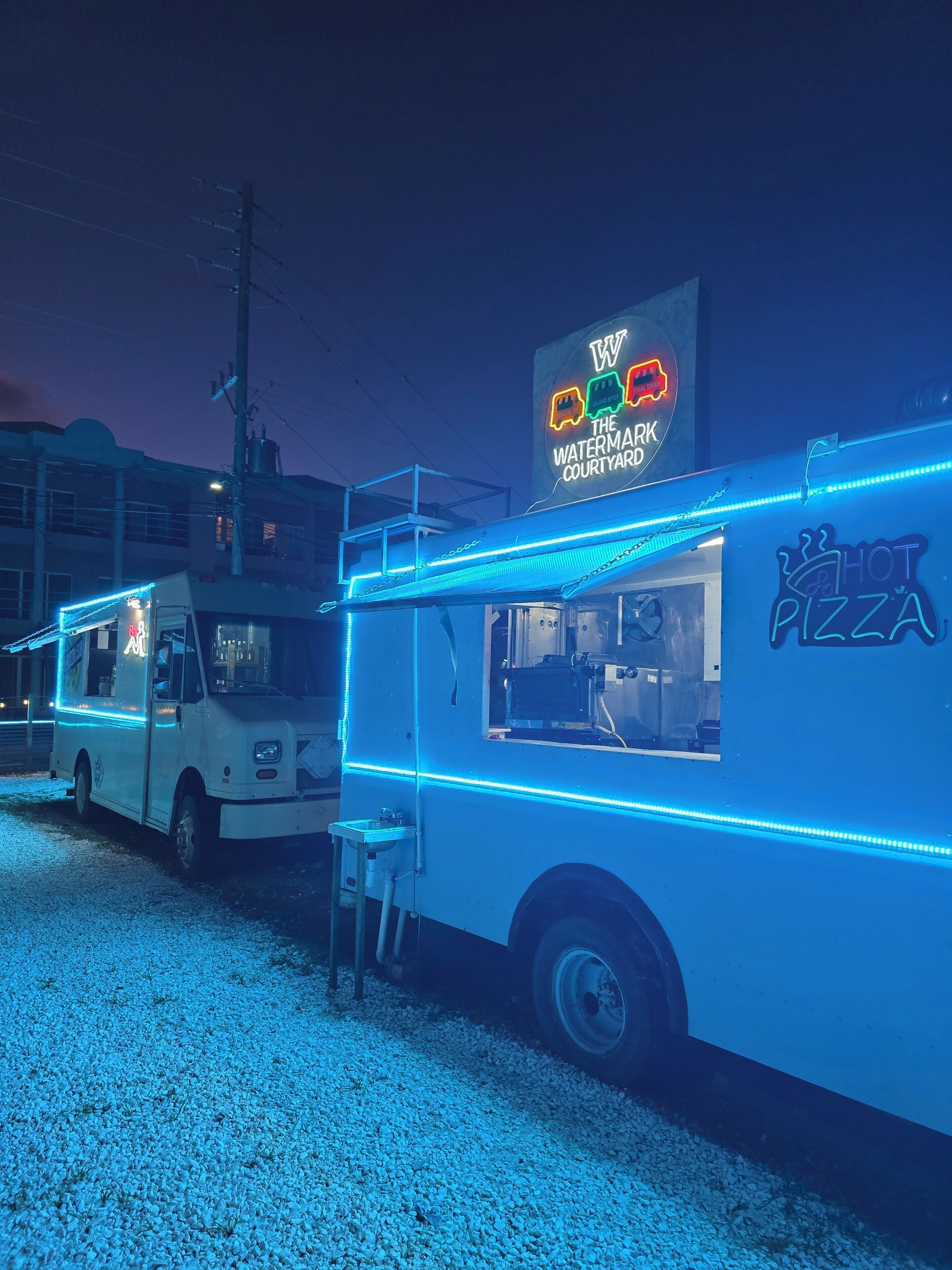 A food truck with neon blue lights and a sign advertising 'HOT PIZZA'.
