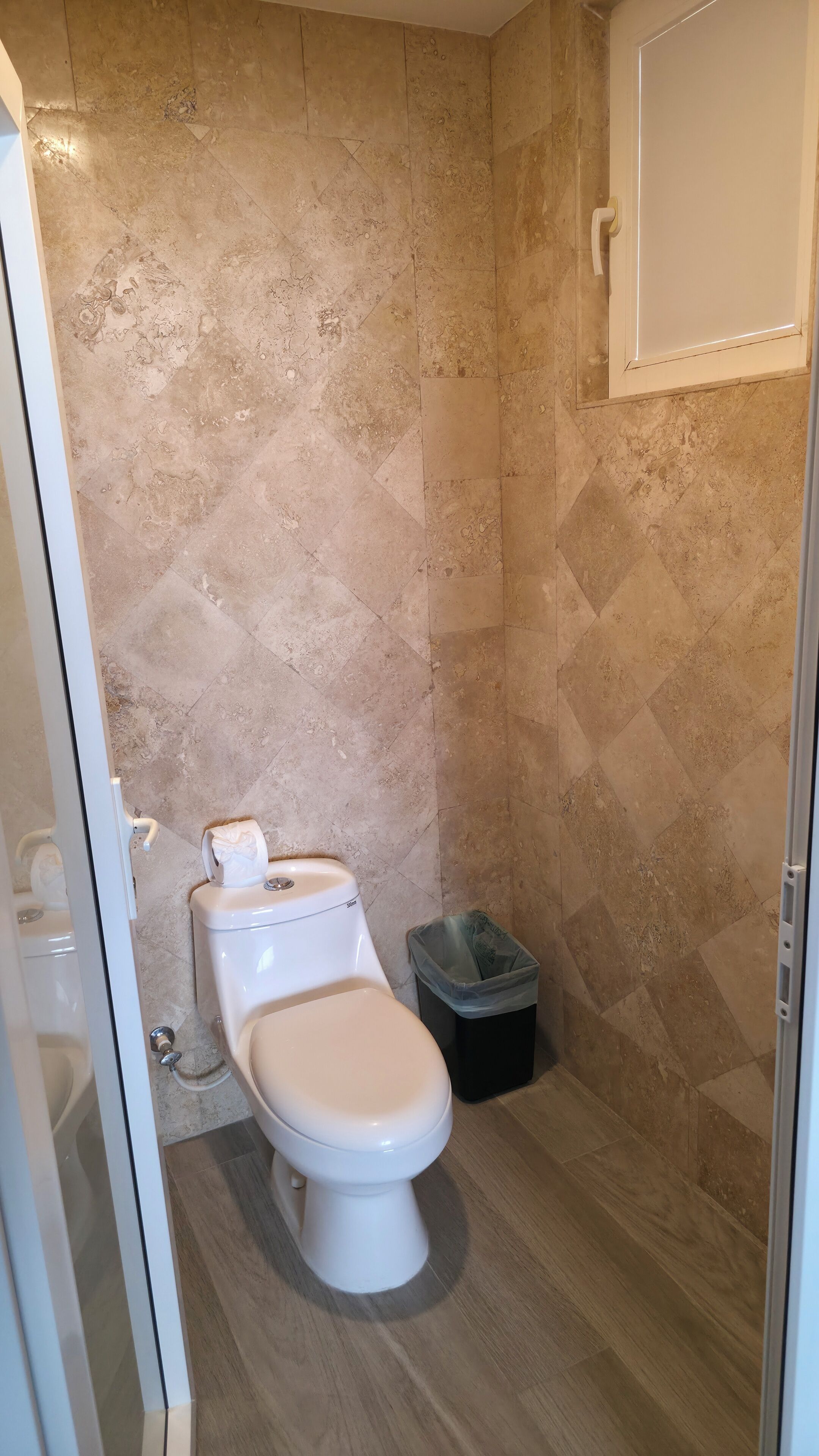 A bathroom with a toilet, a trash bin, and a shower area.