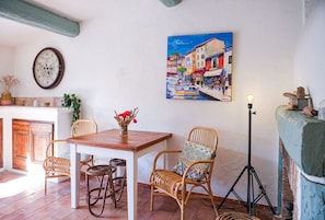 A cozy dining area with a wooden table, wicker chairs, and a painting of a street scene.