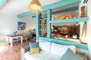 A cozy living room with a sofa, chairs, a dining table, and a kitchen area visible through an open doorway.