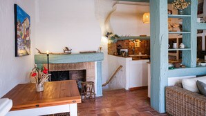 Een gezellige woonkamer met een open haard, een eettafel en een keukenruimte zichtbaar door een boog.