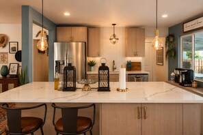 Une cuisine moderne dotée d’un îlot en marbre, d’appareils électroménagers en acier inoxydable et de luminaires suspendus.