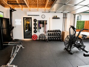 Un gimnasio en casa con equipo de levantamiento de pesas, una cinta de correr y un espejo que refleja el espacio.