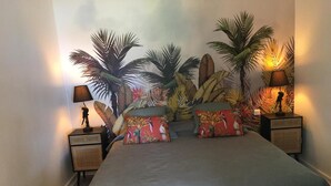 Een slaapkamer met een bed, twee nachtkastjes en een muurschildering van tropische planten.