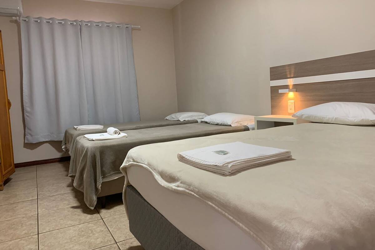 Una habitación de hotel con dos camas individuales, una mesita de noche de madera con lámpara y una ventana con cortinas.
