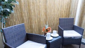 A small outdoor seating area with wicker furniture, a table with a vase of flowers, and a bamboo backdrop.