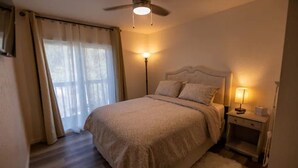A bedroom with a bed, a nightstand, a lamp, a ceiling fan, and a window with curtains.