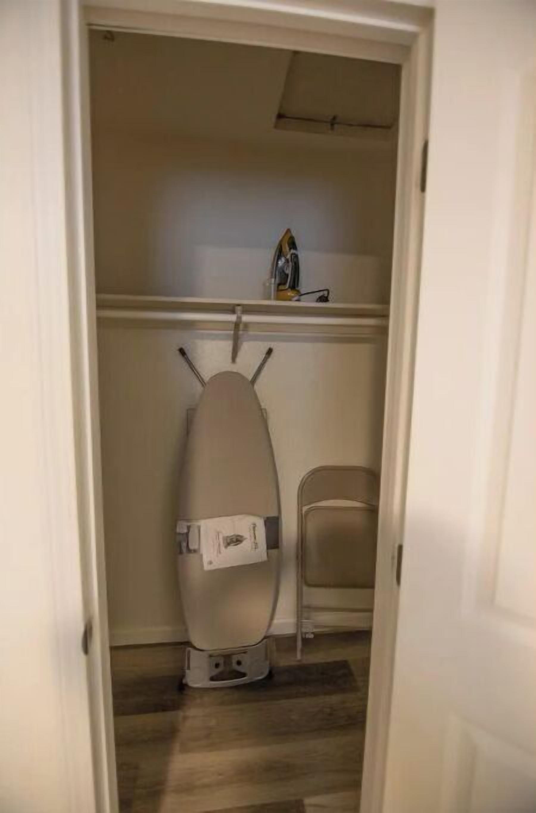 Una habitación con piso de madera, una tabla de planchar blanca y una silla.