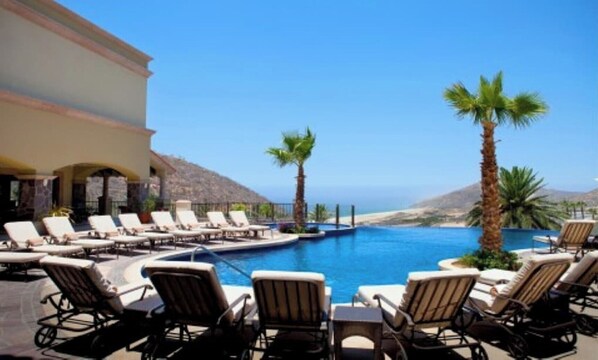 Relax by the oceanfront pool surrounded by palm trees and lounge chairs.