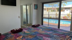 Een slaapkamer met een bed, een schuifdeur naar een zwembad en uitzicht op het zwembad.