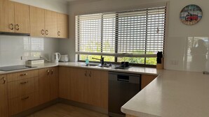 Een moderne keuken met houten kastjes, een vaatwasser, een spoelbak en een raam met zonwering.