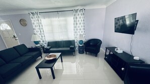 Un salon avec un canapé, une table basse, un téléviseur et un fauteuil.