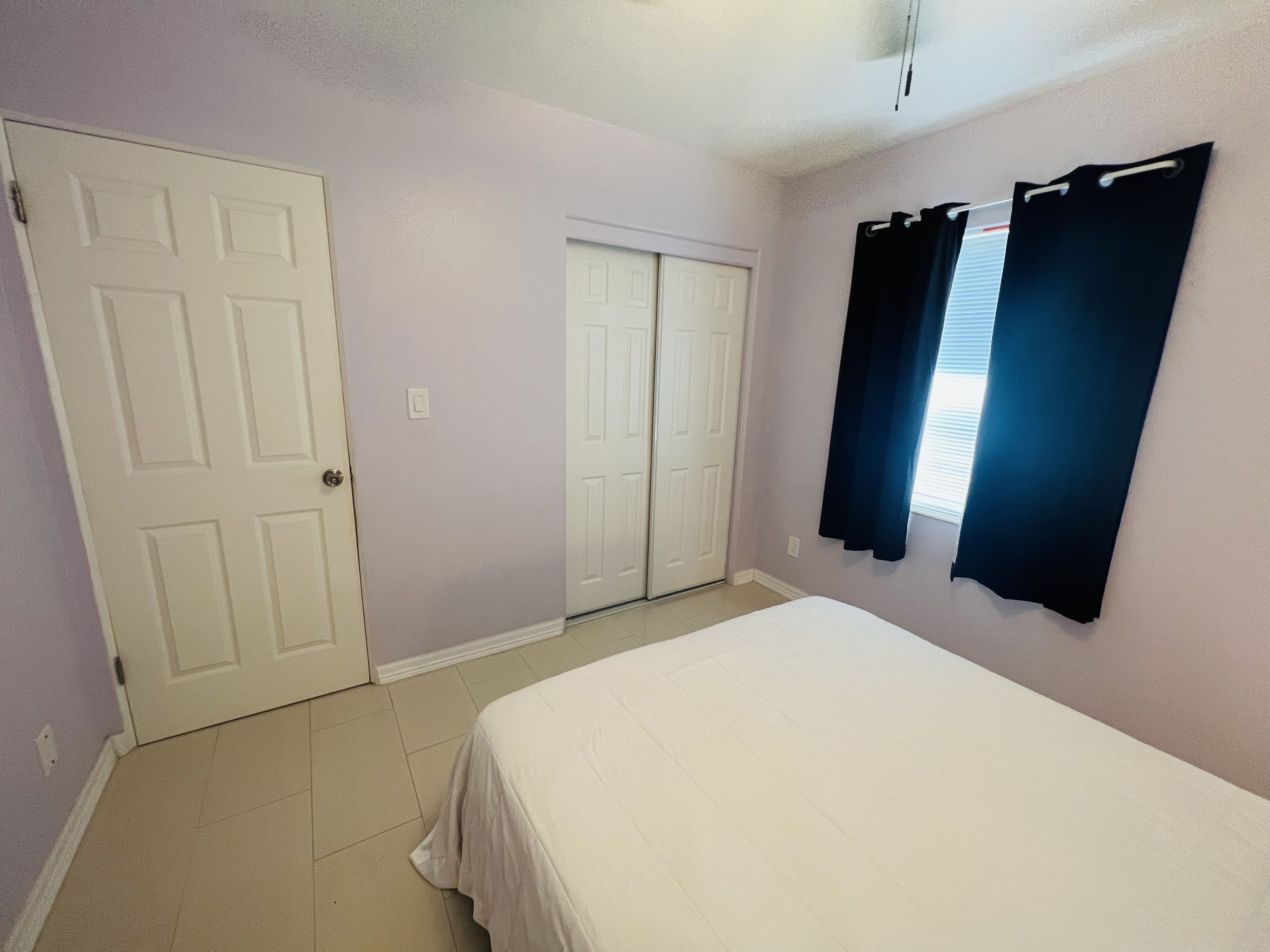 A bedroom with a bed, two doors, and a window with curtains.